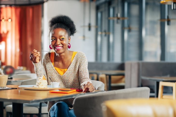 A happy woman smiles while eating a slice of pie in a restaurant