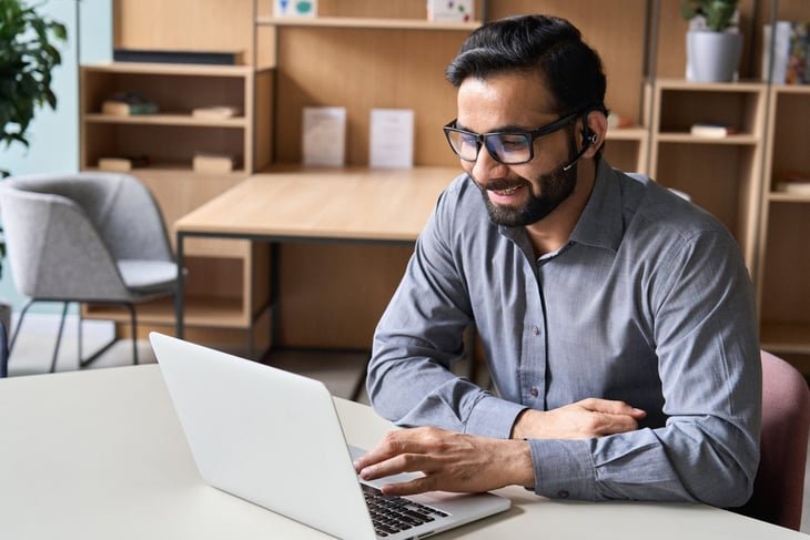 businessman wearing glasses and headset having virtual team meeting on his laptop