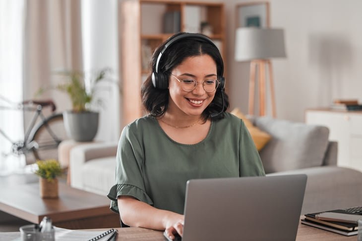 Happy, smiling woman working on a laptop, wearing headset. Virtual assistant.