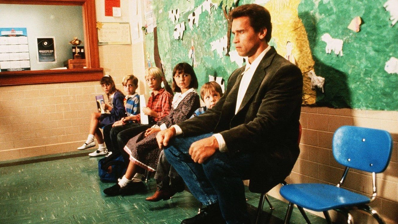 Arnold Schwarzenegger sitting next to small kids in an office in Kindergarten Cop