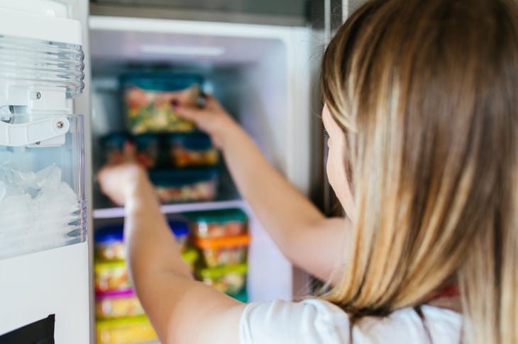 Woman placing container with frozen mixed vegetables in freezer.