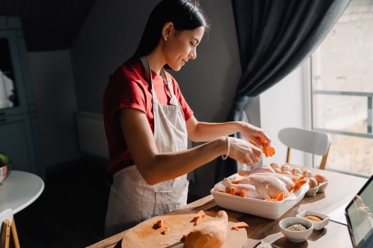 A woman using tablet-computer while preparing a chicken to roast in a home kitchen
