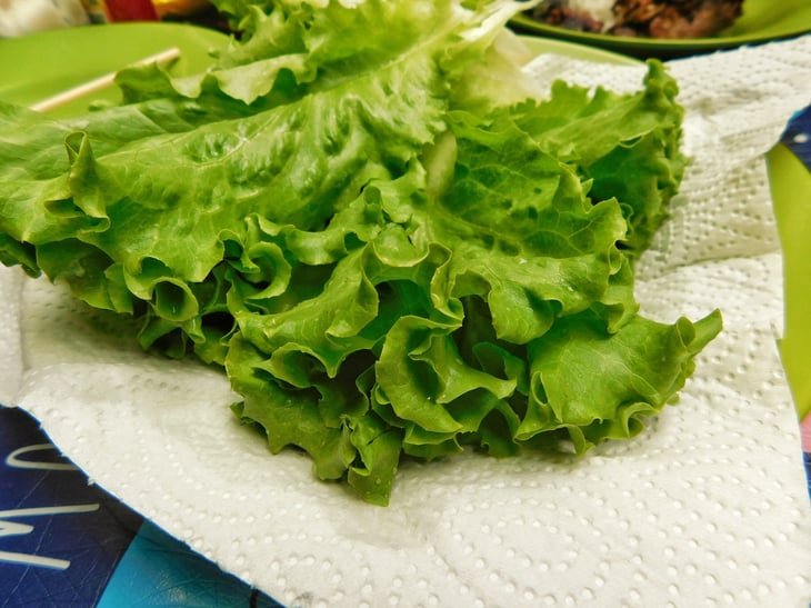 Fresh green lettuce leaves with crisp, curly edges, placed on a white paper towel.