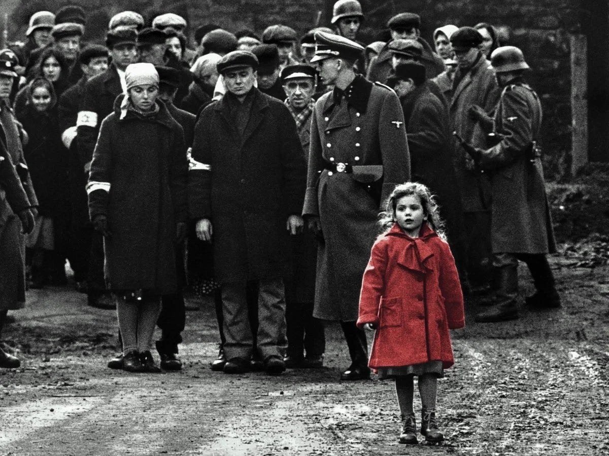 Girl in red coat standing around adults in Schindler's List