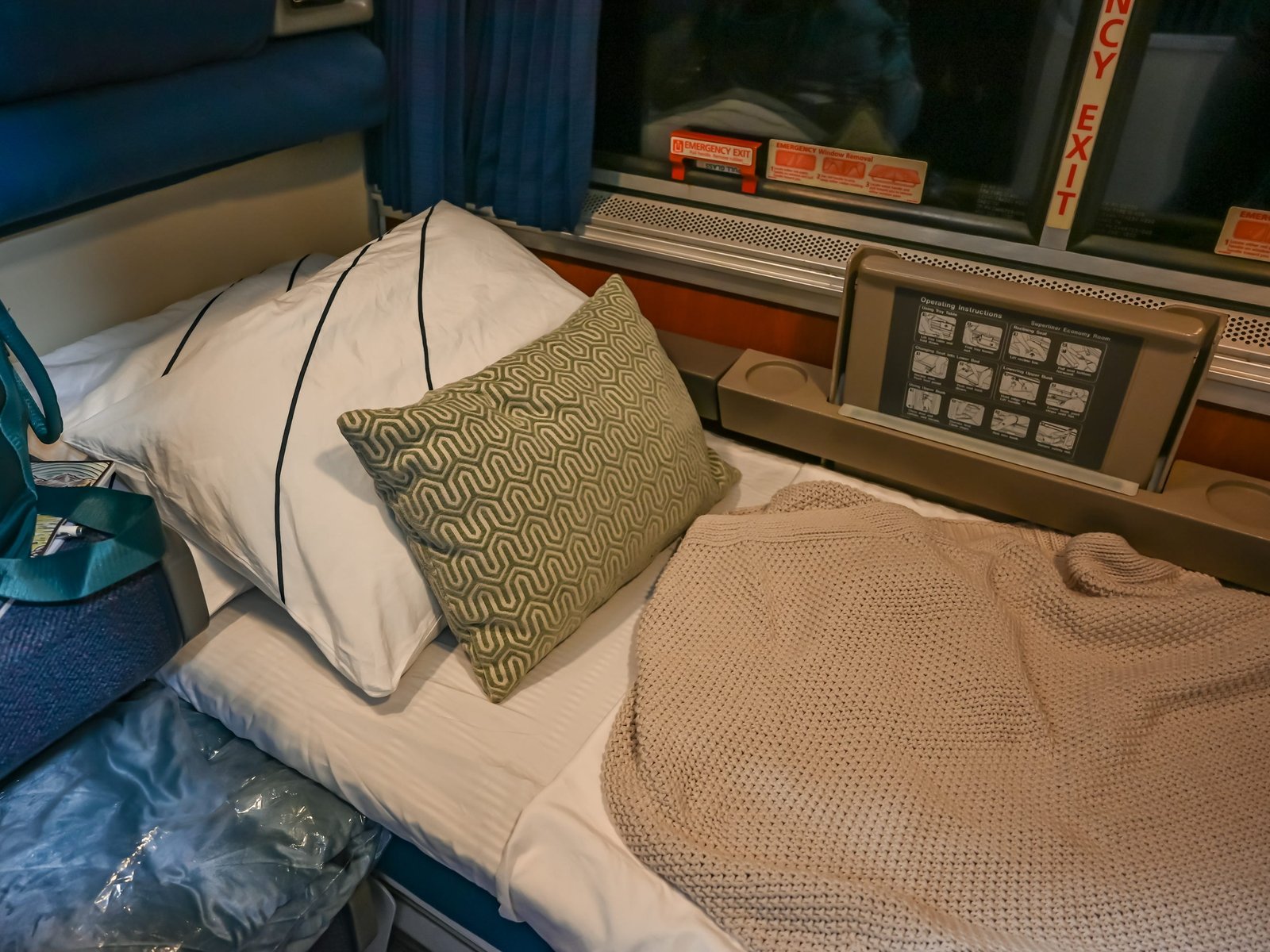 Roomette bed with green and white pillows and tan blanket