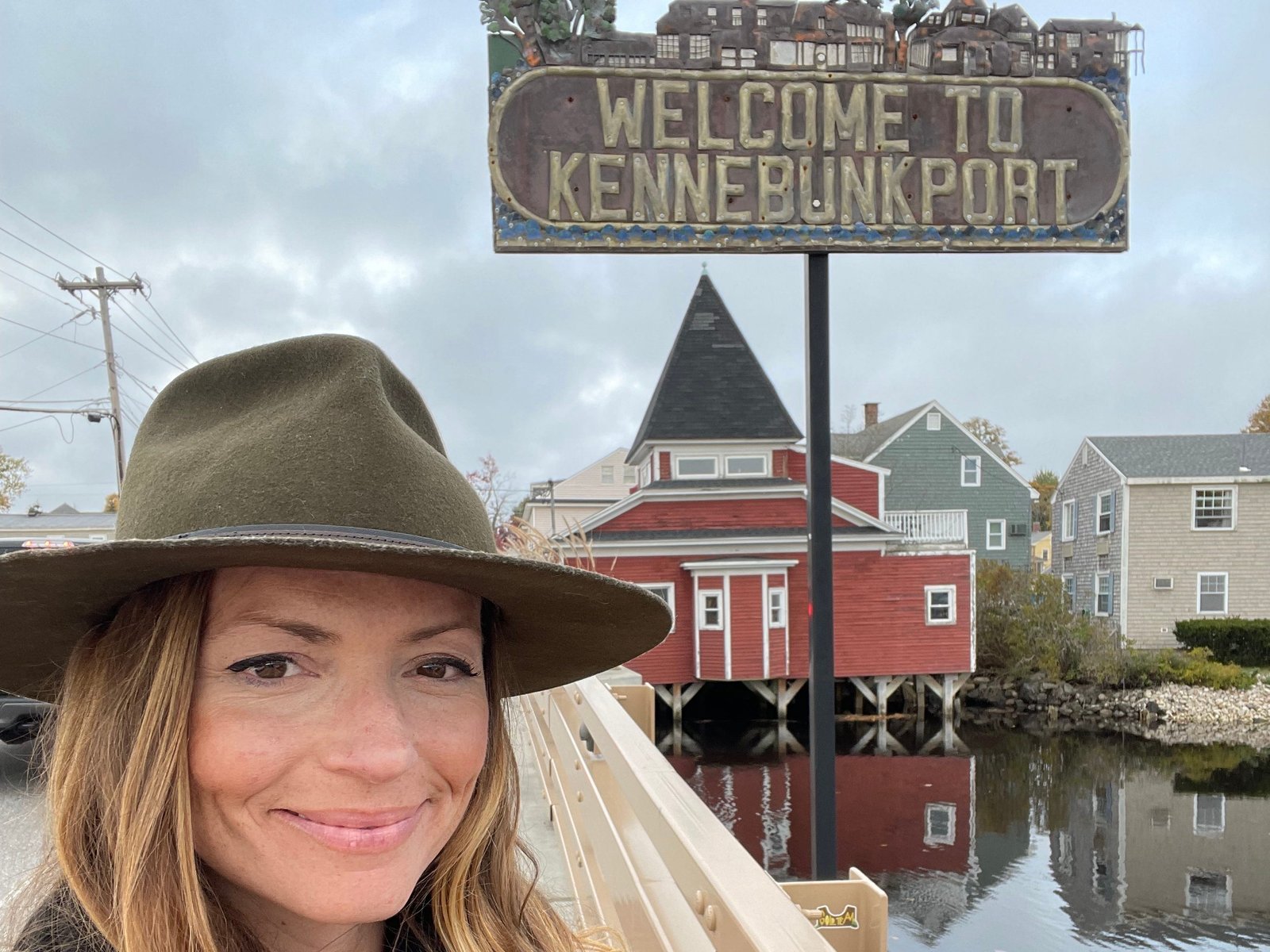 Emily taking a selfie in front of a sign that says "Welcome to Kennebunkport" alongside the water.