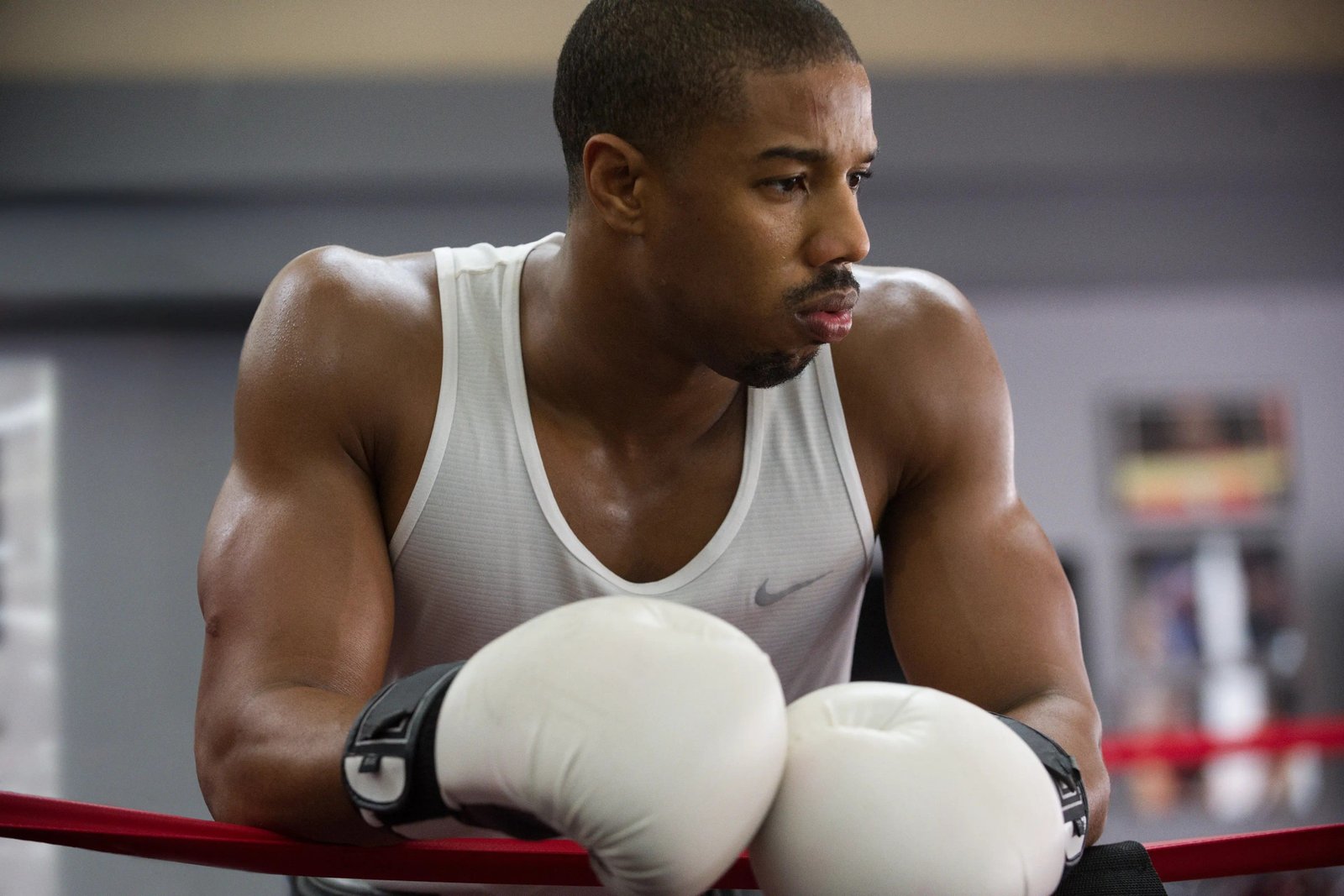 Michael B. Jordan wearing boxing gloves leaning on boxing ring ropes
