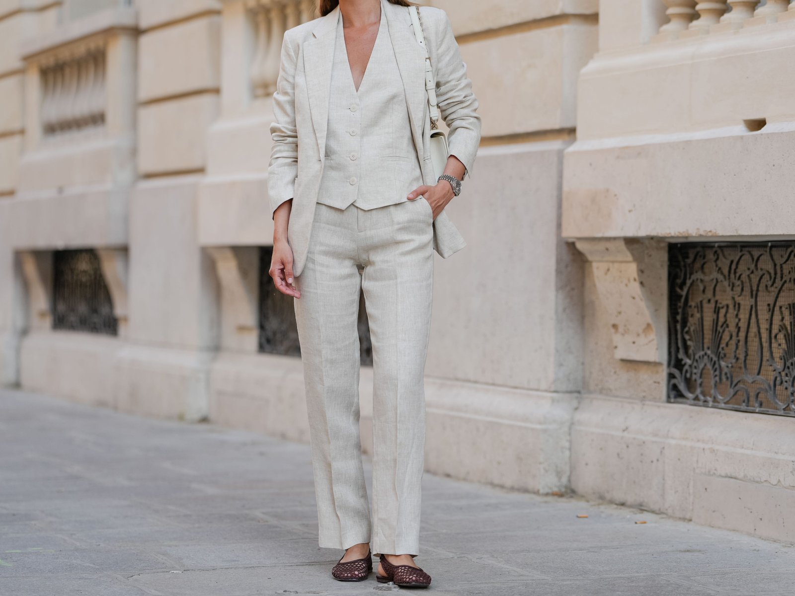 A woman wears a beige linen vest, pants, and a blazer.