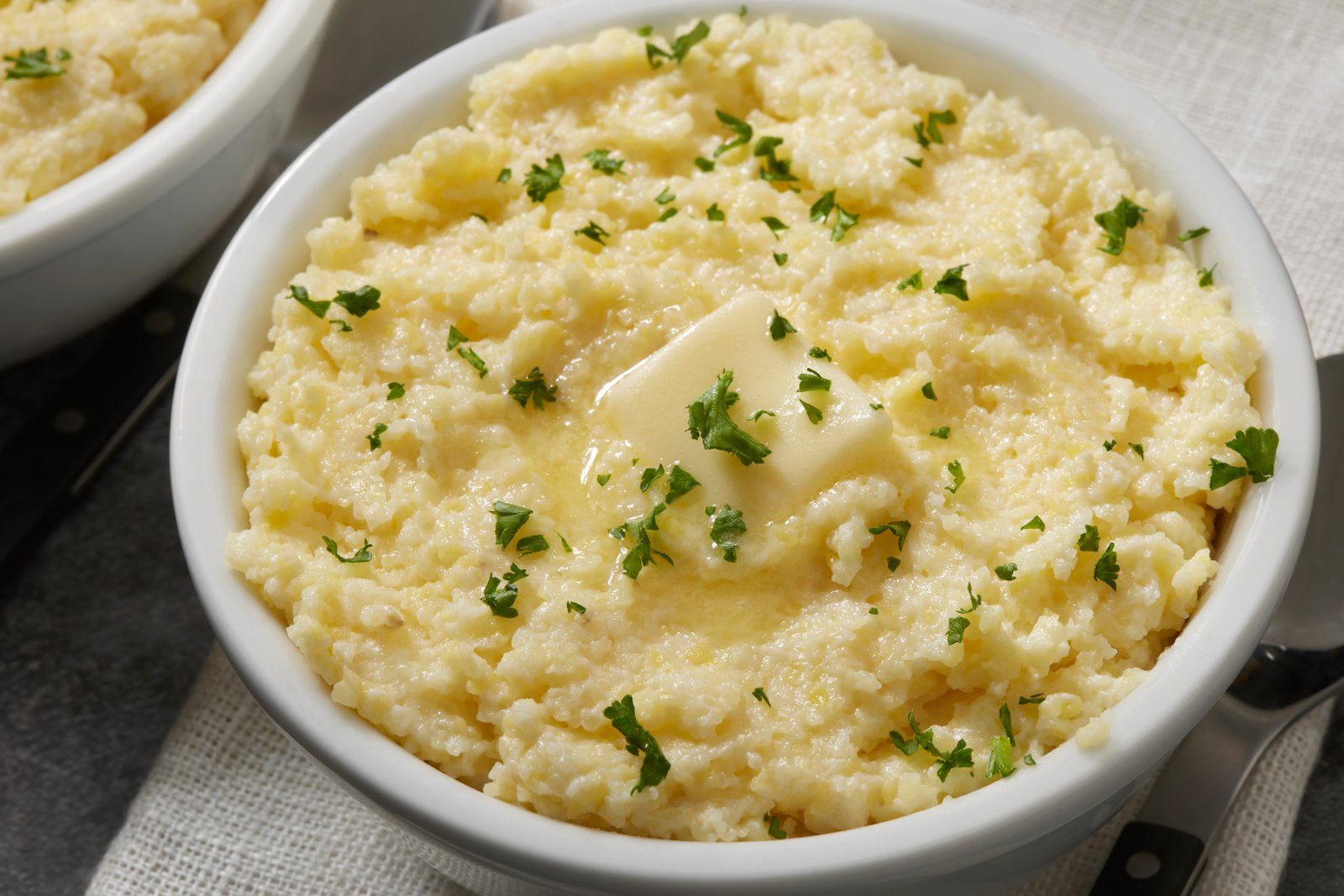 Bowl of mashed potatoes topped with pat of butter and herbs