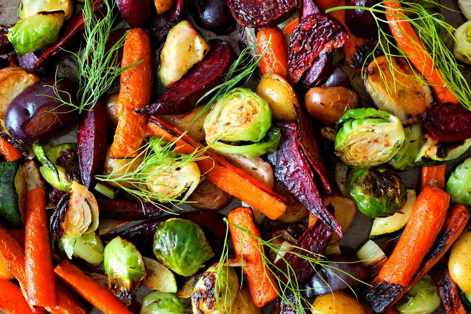 Roasted vegetables like beets, carrots, and Brussels sprouts on a pan.