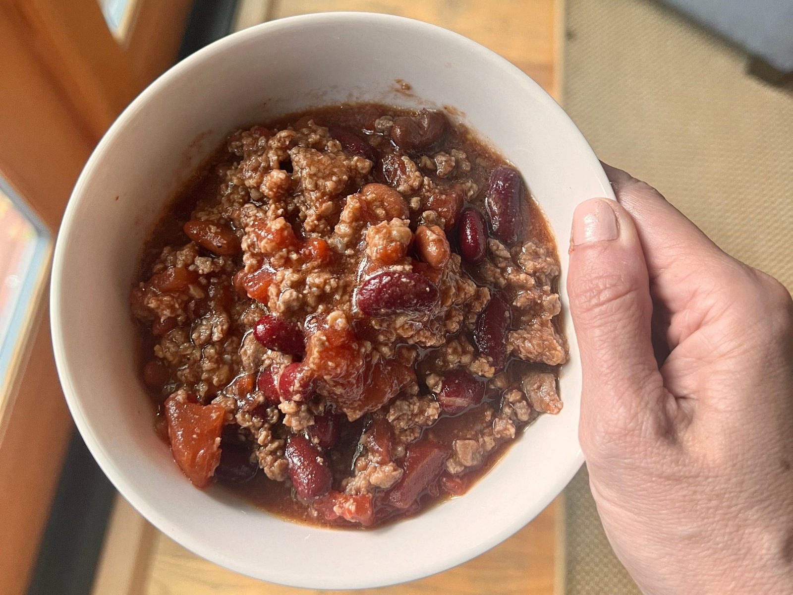hand holding up a bowl of meat and bean chili