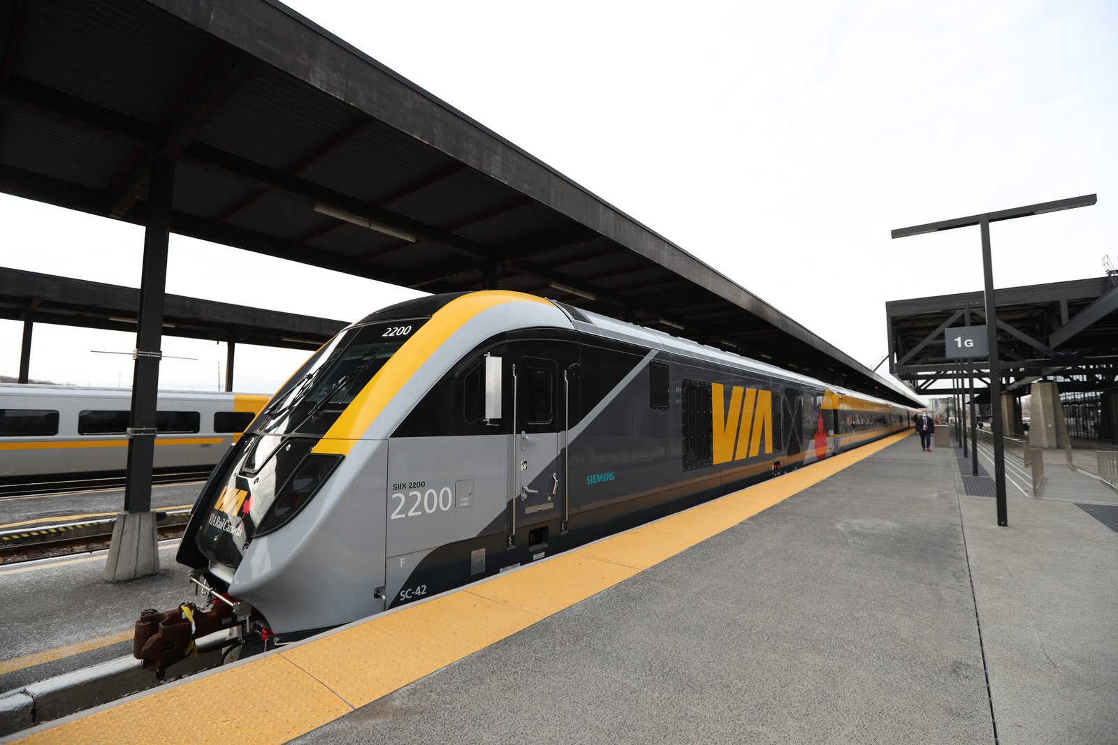 A VIA Rail train numbered 2200 stands beside a station platform under a dark canopy.